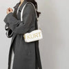 A woman holds a white leather tote bag with gold lettering against a gray coat.