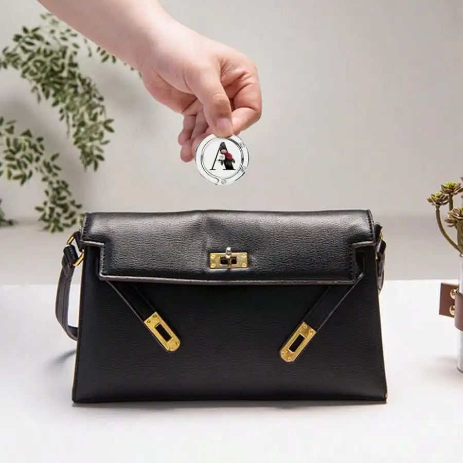 A black leather foldable letter hanger hook is being held over a black leather clutch purse.
