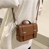 A brown minimalist leather crossbody bag worn by a person, featuring a leather strap and silver hardware.