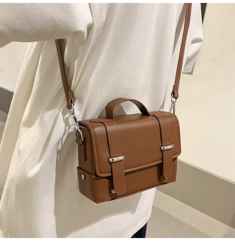 A brown minimalist leather crossbody bag worn by a person, featuring a leather strap and silver hardware.