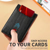 A black carbon fiber wallet with a thumb hole for easy card access is held by a hand.