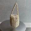 A cream-colored beaded clutch bag hanging by its strap against a light gray background.