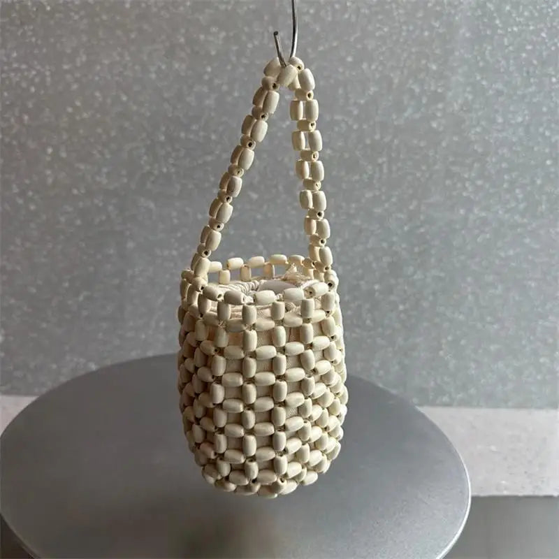 A cream-colored beaded clutch bag hanging by its strap against a light gray background.