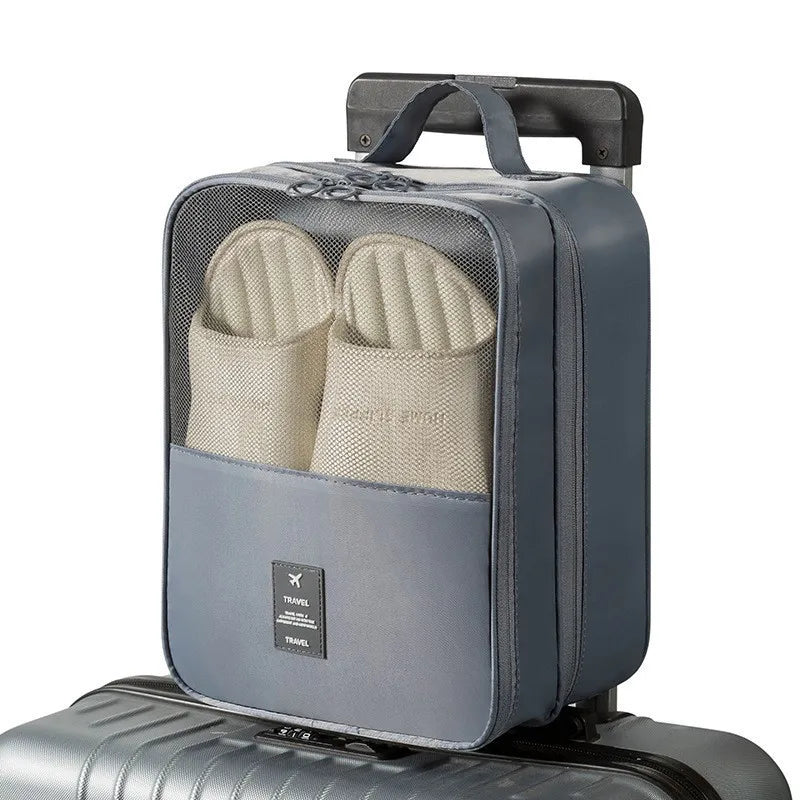 A gray portable luggage shoe organizer bag with multiple compartments resting on a silver suitcase.