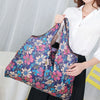A woman holds a purple and pink floral patterned foldable water-resistant shopping tote bag.