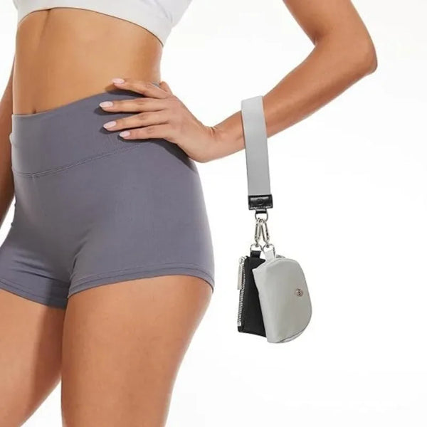 A person wearing gray athletic shorts holds a silver wristlet wallet with a black strap.