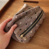 Une main tient une pochette de rangement cosmétique en tissu gris à pois noirs et une fermeture éclair dorée sur une surface 