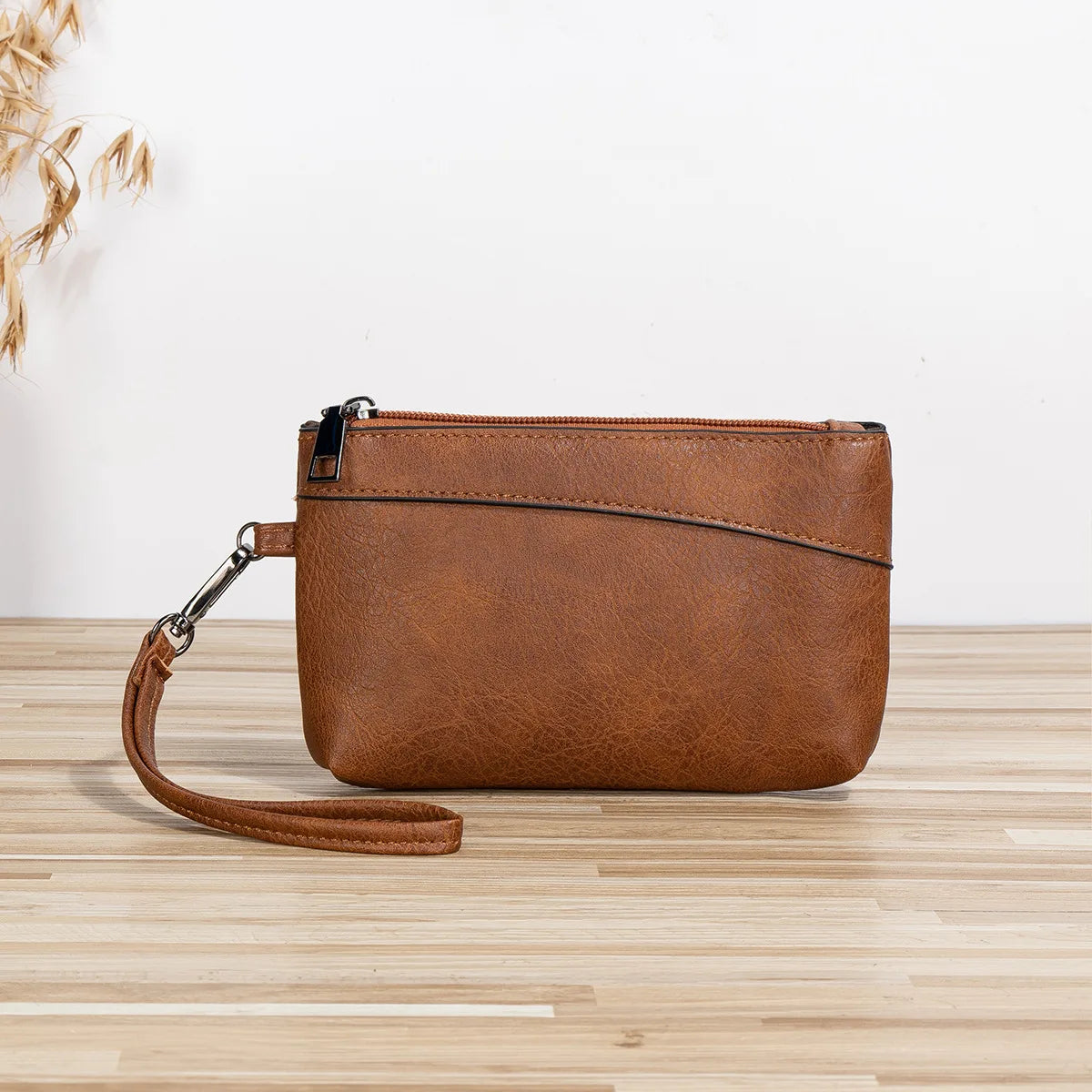A brown retro PU leather zipper wrist bag resting on a light wooden surface.