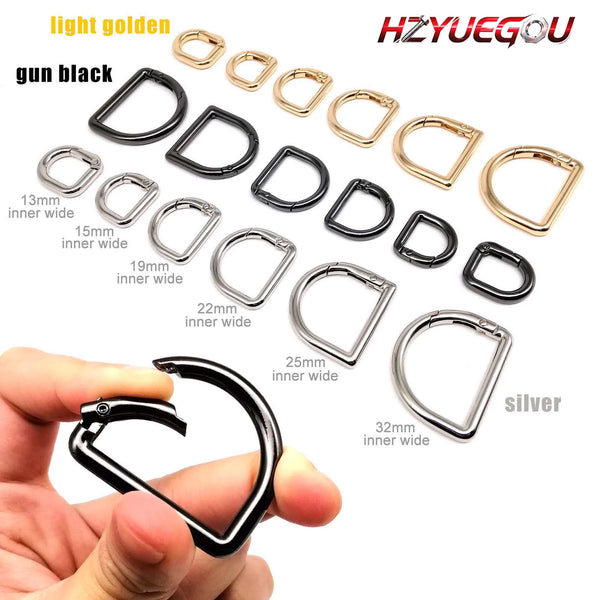 A collection of gold and black D-shape metal spring rings and clasps with various inner widths shown next to a hand.