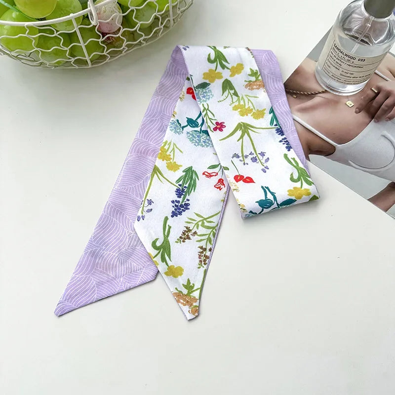 Un foulard pour les cheveux en soie violet avec un motif floral blanc, exposé à côté d'une bouteille en verre.