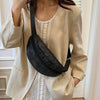 A woman is holding a beige blazer over a light-colored dress and carrying a black rhinestone-embellished crossbody bag.