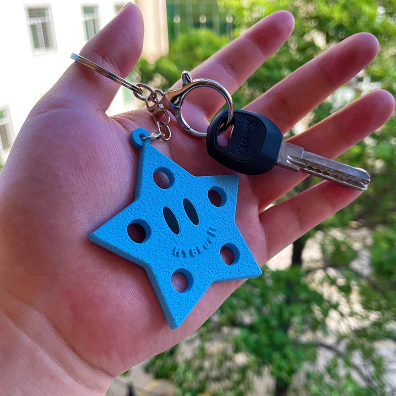Une main tient un porte-clés de chaussure en silicone en forme d'étoile bleu vif avec un anneau argenté attaché à une clé noi