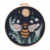 A circular embroidery hoop featuring a dark background with a large moon and detailed floral elements, designed for a butterf