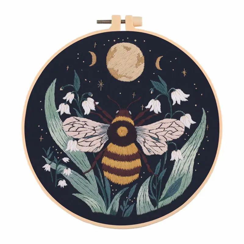 A circular embroidery hoop featuring a dark background with a large moon and detailed floral elements, designed for a butterf