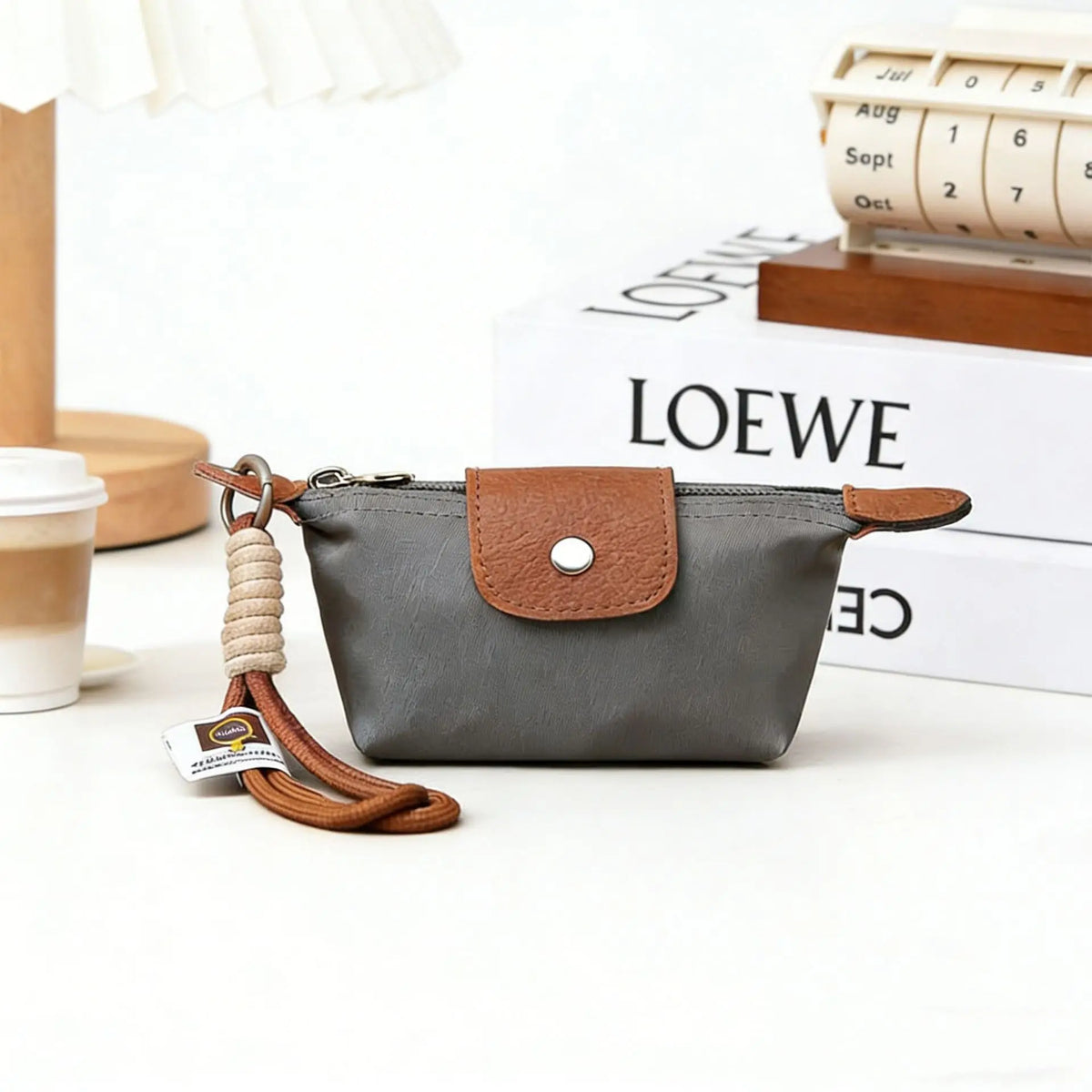 A gray compact coin purse made of nylon and faux leather with a brown leather strap and keychain.