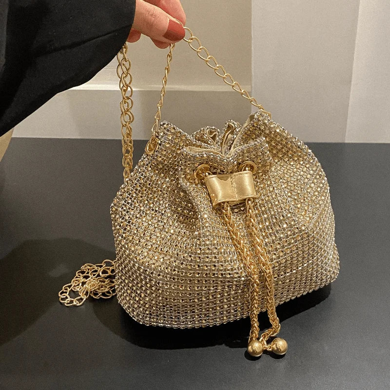 Primer plano de una bolsa de cruz con cordón y pedrería brillante dorada, sostenida por una mano.