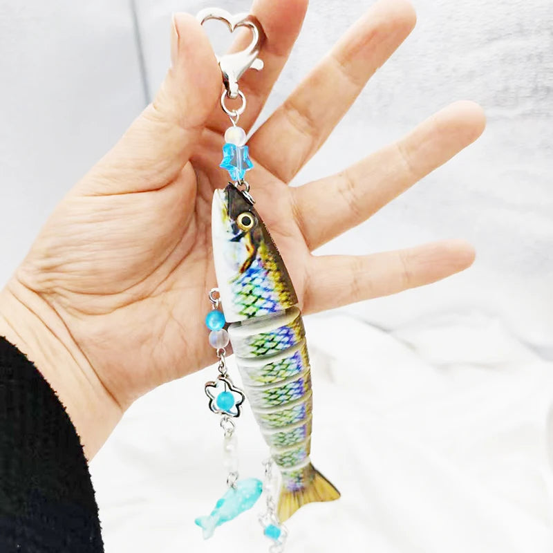 A hand holds a silver fish-themed acrylic keychain charm with blue accents.