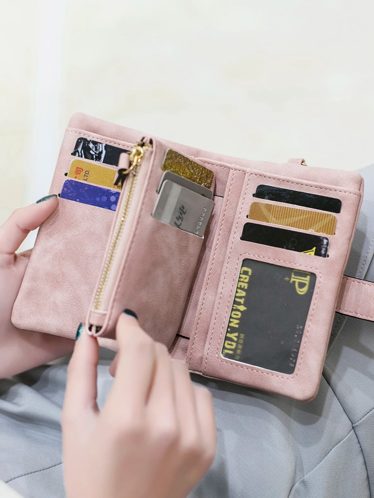 A hand is opening a pink multi-slot frosted card wallet displaying various credit cards and an ID.