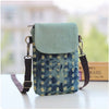 A teal denim mini messenger bag with a light green flap and brown leather strap resting on a white surface.