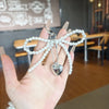 A hand holds a Y2K bowknot pearl keychain with a silver heart charm and pearl strands.