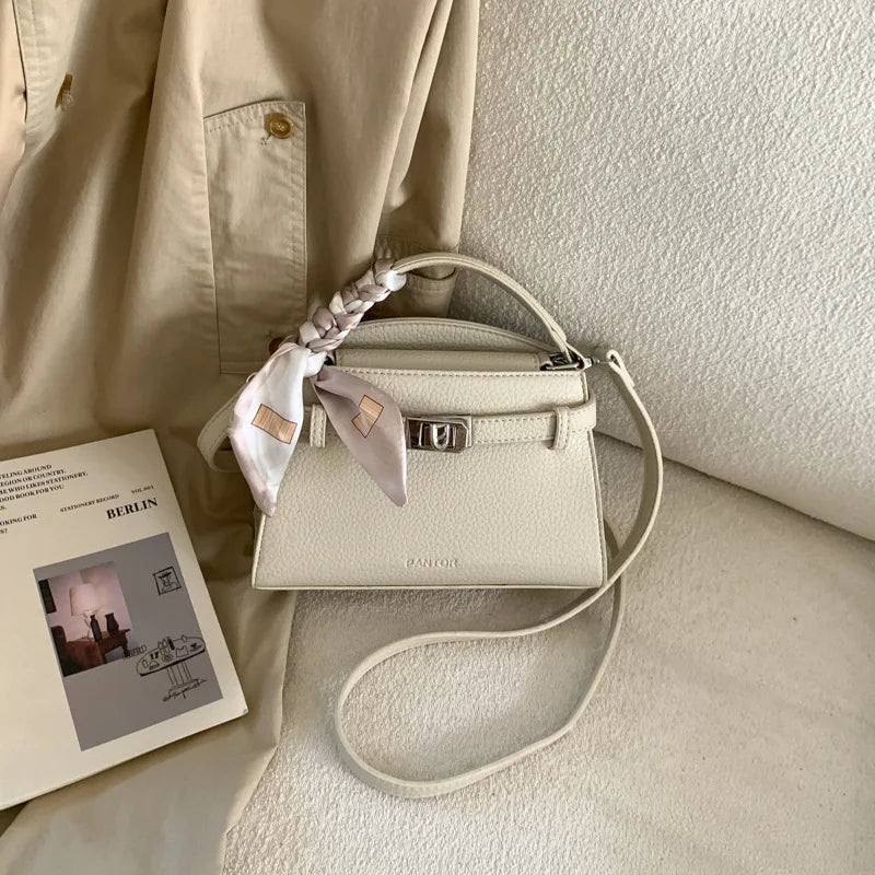 A beige elegant PU leather crossbody clutch bag with a woven strap resting on a light colored fabric.