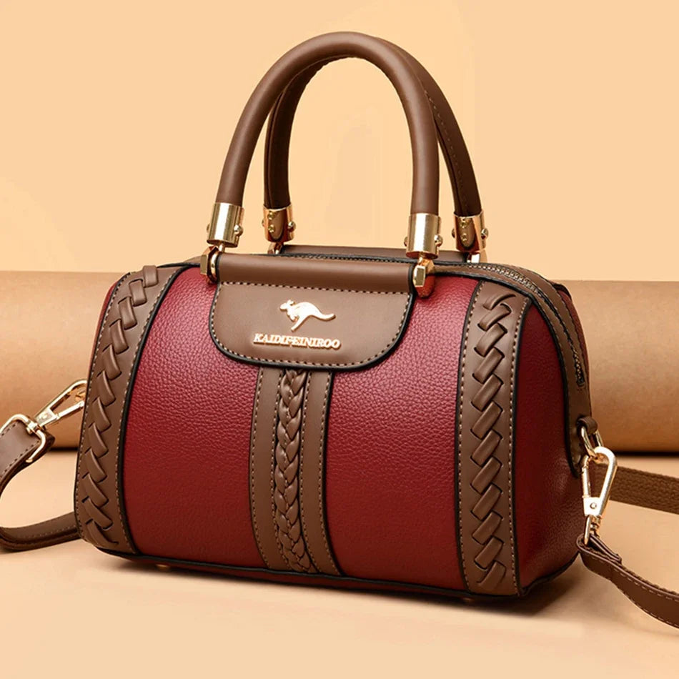 A maroon leather shoulder bag with brown stitching and gold hardware resting on a beige surface.
