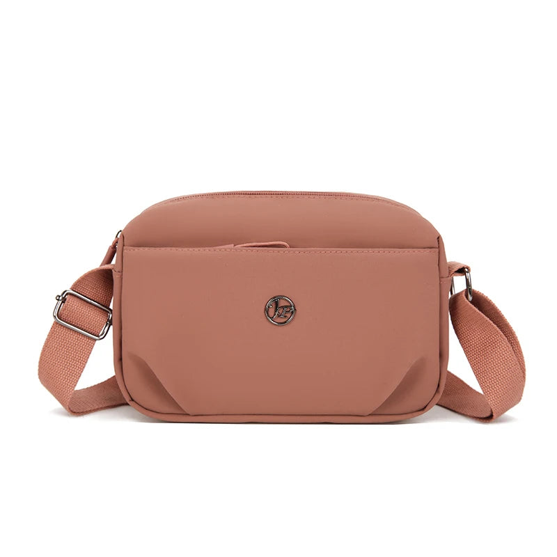 Bolso cruz impermeable de nylon color rosa polvoriento claro con solapa y correa ajustable.