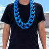 A man wearing a black t-shirt and a bright blue acrylic Cuban link necklace.
