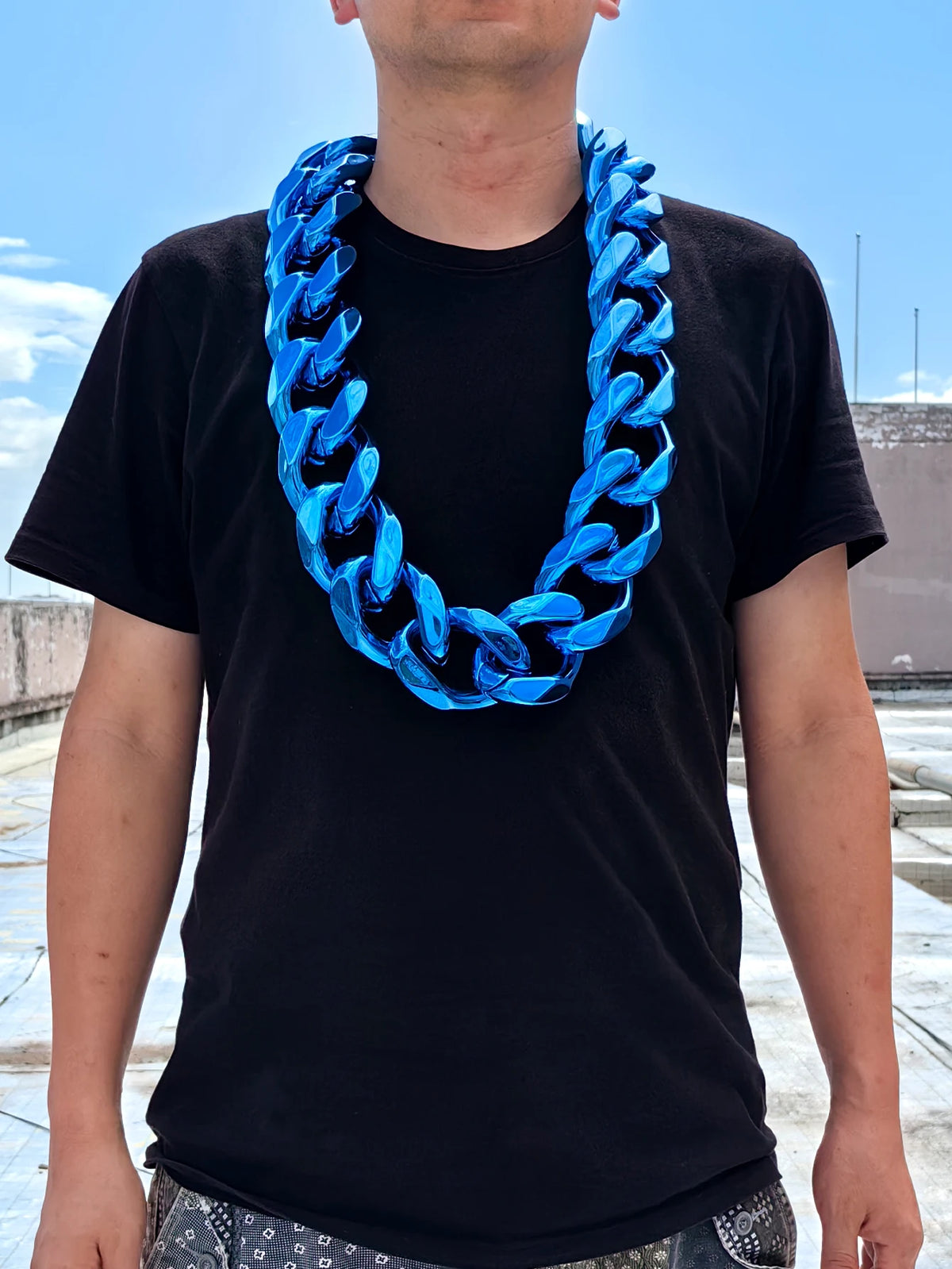 A man wearing a black t-shirt and a bright blue acrylic Cuban link necklace.