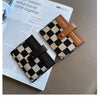 A checkered black and tan PU leather mini card wallet with a brown leather strap resting on a white paper.