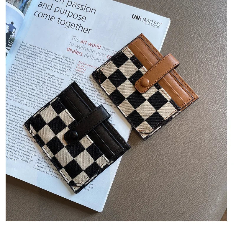A checkered black and tan PU leather mini card wallet with a brown leather strap resting on a white paper.