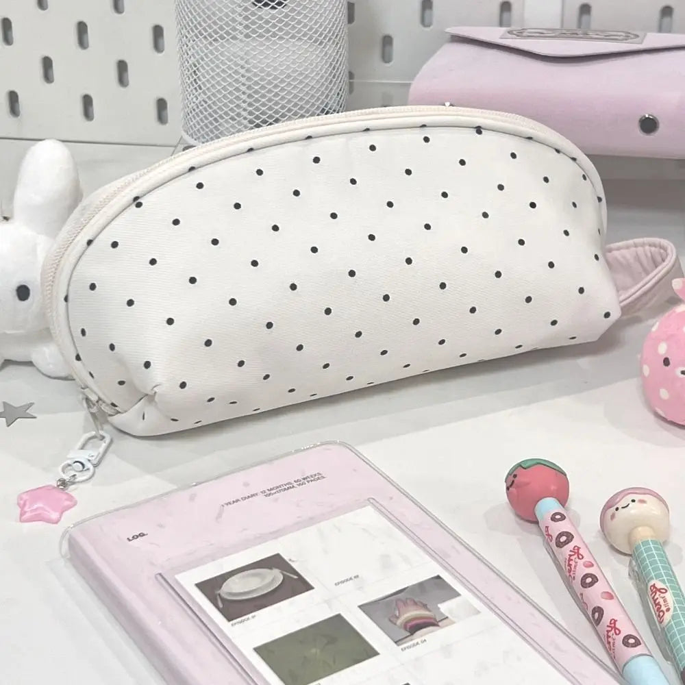 A white polka dot shell pencil case next to a pink pencil case and a small pink item.
