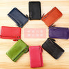 Eight genuine leather wristlet clutch wallets in various colors arranged in a circle on a wooden surface.
