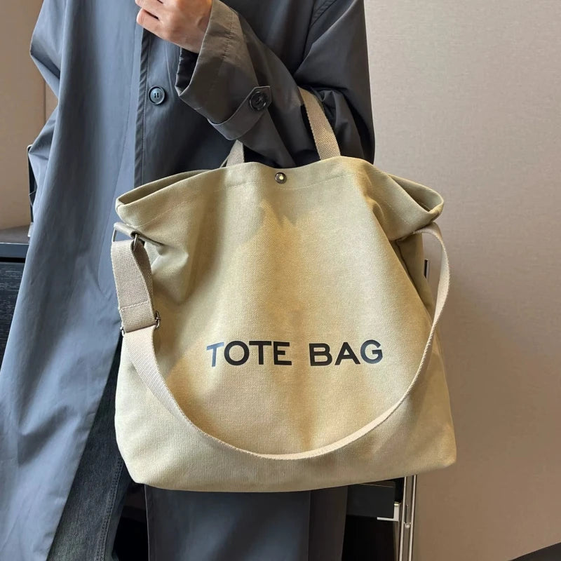 A person holds a beige canvas tote bag with the text TOTE BAG against a light gray background.