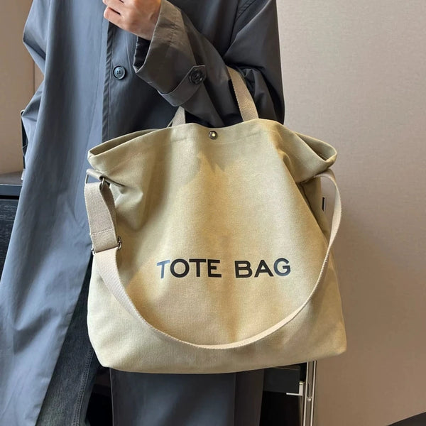 A person holds a beige canvas tote bag with the text TOTE BAG against a light gray background.