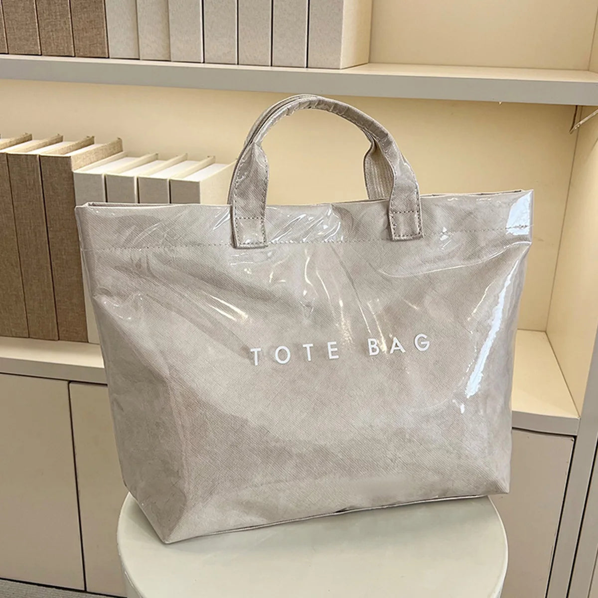 Una bolsa de tela minimalista de PVC gris claro con asas exhibida en un estante.