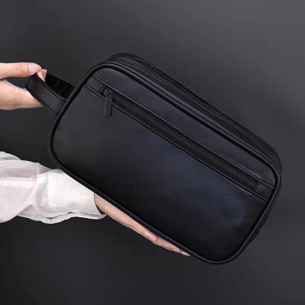 Une main tient un sac de toilette en cuir PU noir à fermeture éclair ouverte, vue de dessus.