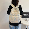 A light cream nylon backpack with a blue bow print, worn by a person against a white wall.