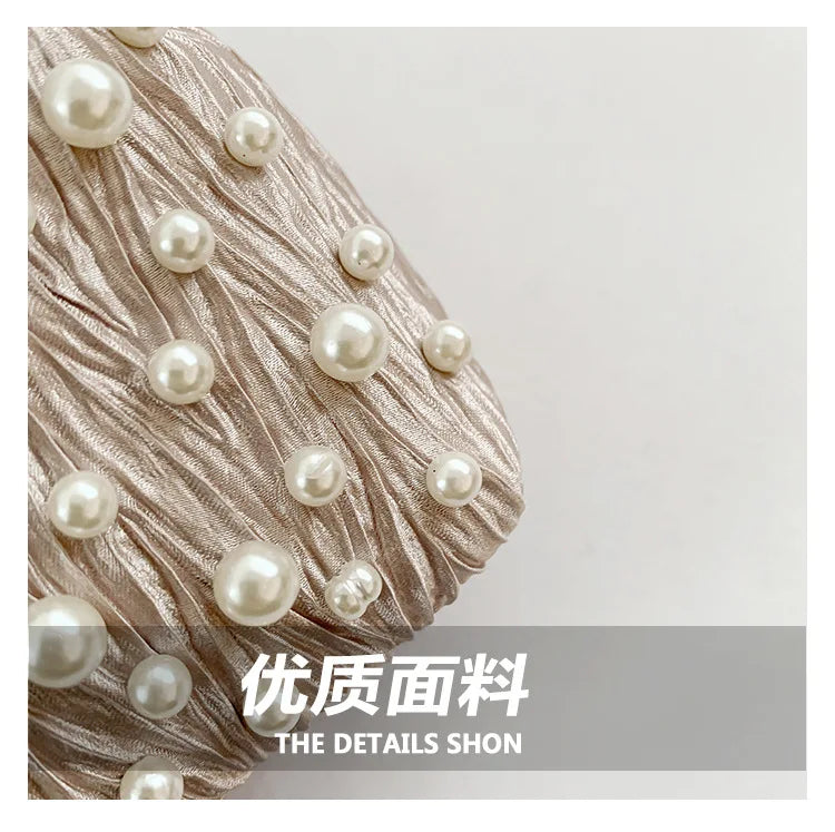 Close-up of a beige silk fabric embellished with small white pearls, showing the texture and detail.