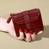 A hand holds a maroon PU leather card wallet with a double zip closure.