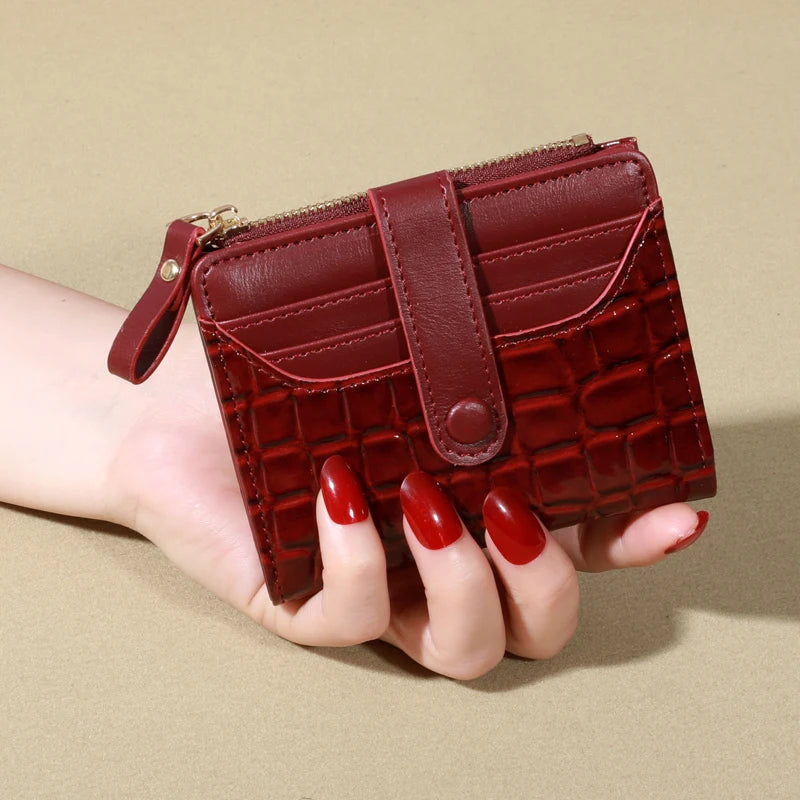 A hand holds a maroon PU leather card wallet with a double zip closure.