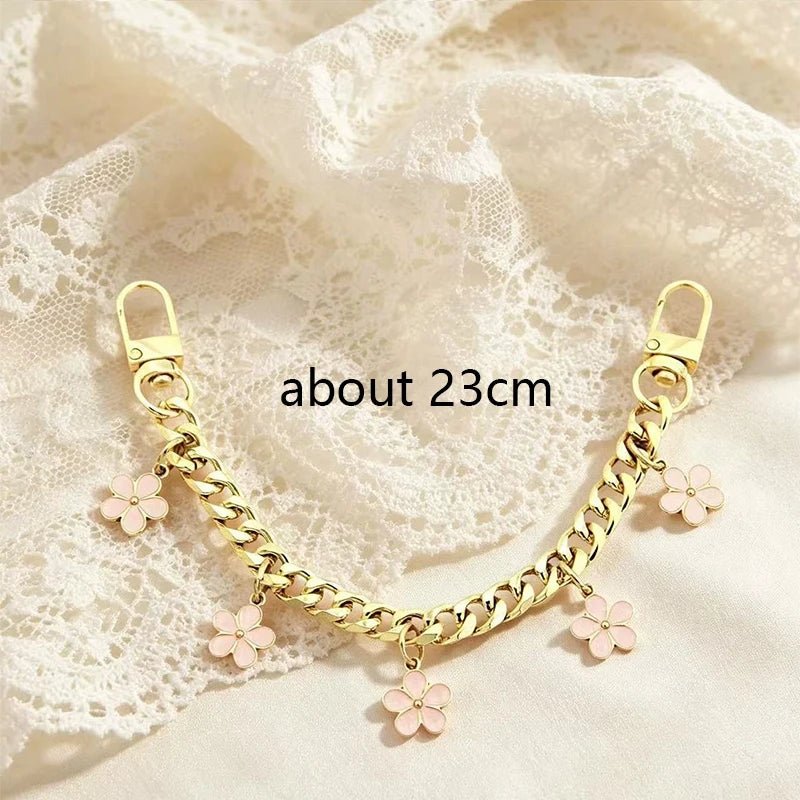 Gold chain necklace with pink flower charms draped on a sheer white fabric background.