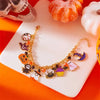 A gold charm bracelet featuring Halloween themed charms like pumpkins, ghosts, and bats displayed on a white surface.