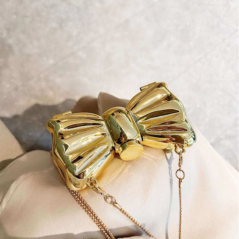 A golden bow knot bag with a detachable gold chain strap resting on a light fabric.