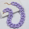A purple matte acrylic choker necklace with a gold-tone chain is displayed on a white surface.