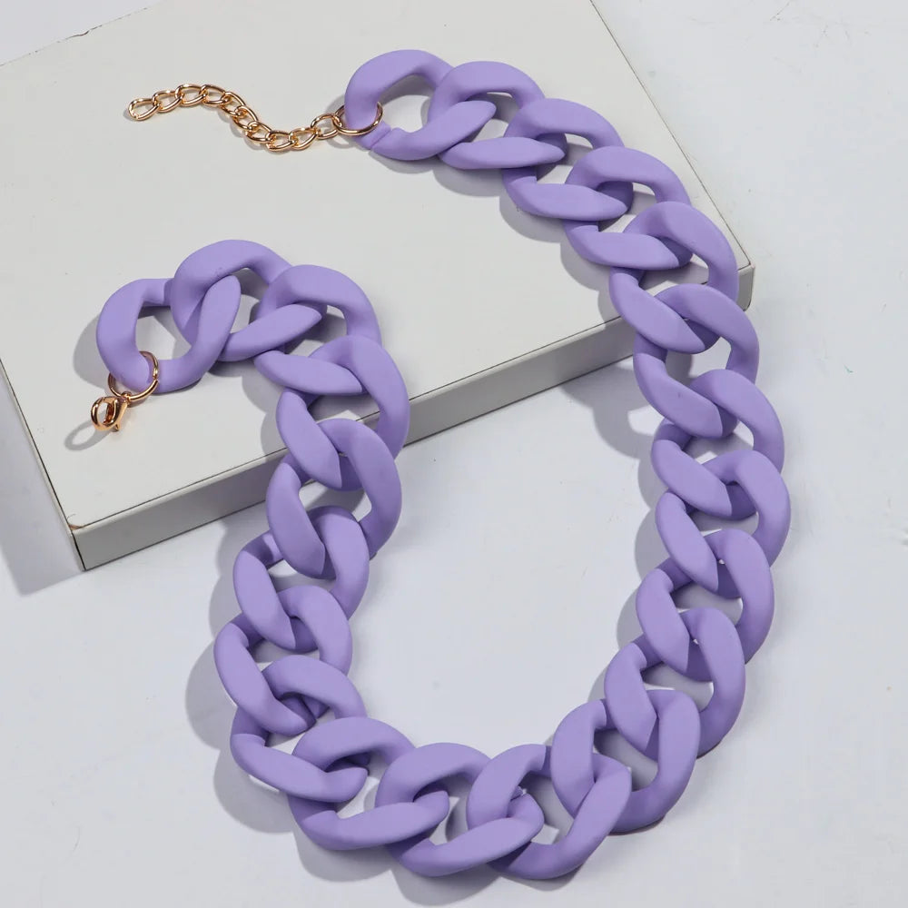 A purple matte acrylic choker necklace with a gold-tone chain is displayed on a white surface.