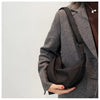 A woman wearing a brown tweed jacket is holding a black sling crossbody bag.