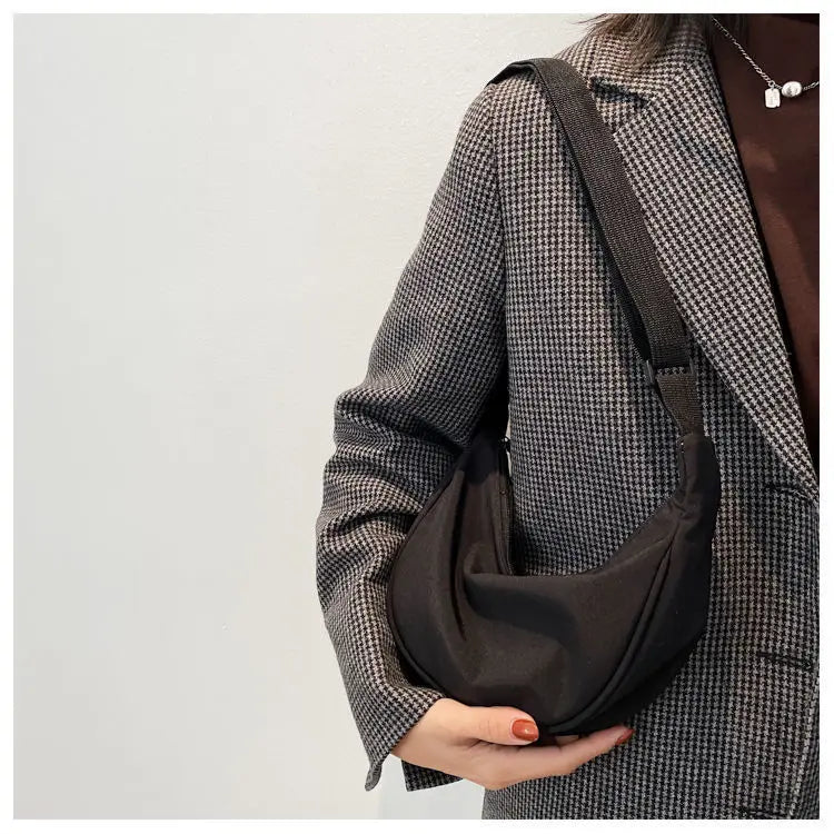A woman wearing a brown tweed jacket is holding a black sling crossbody bag.