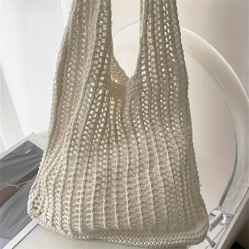A beige knit shoulder bag with a textured, openwork pattern is displayed on a white surface.