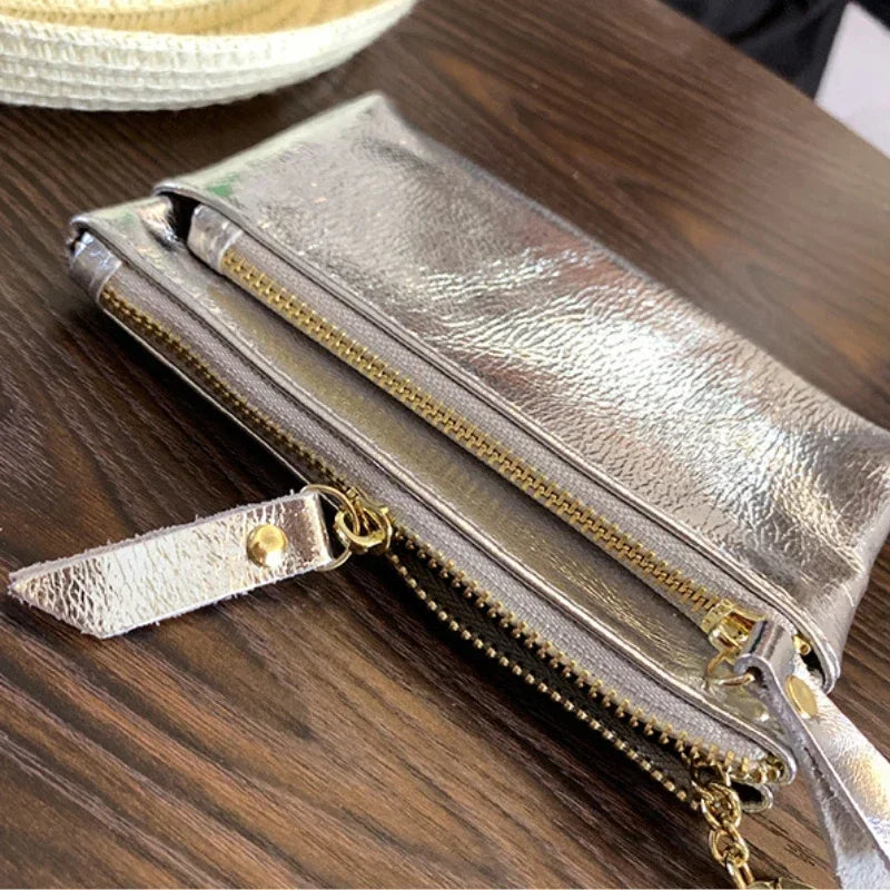 A silver metallic leather compact coin purse and key holder resting on a dark wooden surface.